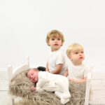 Two older brothers having their photos with their newborn baby brother all sleepy.